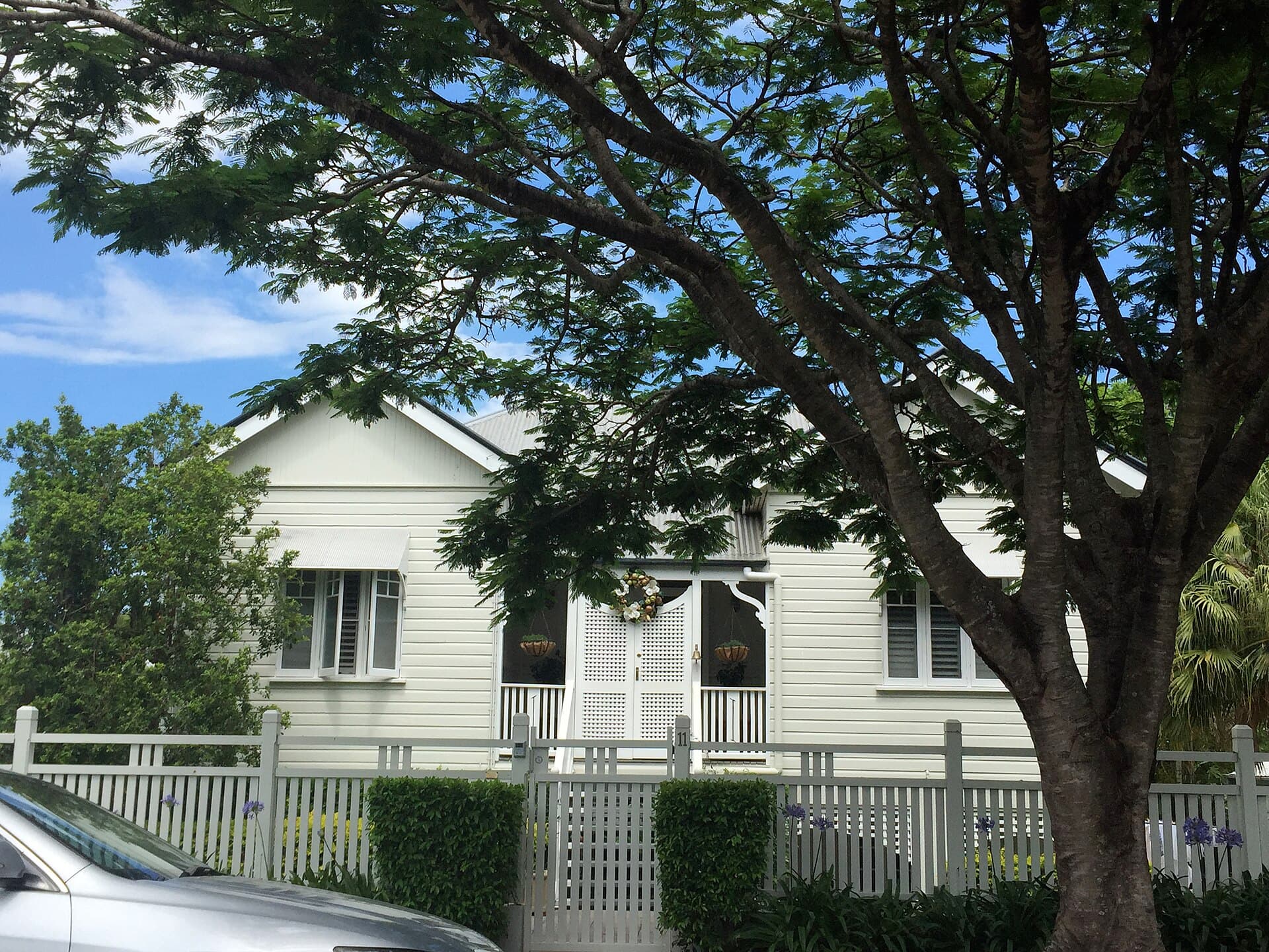 White Queenslander cottage in Ascot behind a low picket front fence and a self-closing pedestrian gate, the sort of everyday gate geometry that becomes critical when the same hardware is asked to protect a pool.