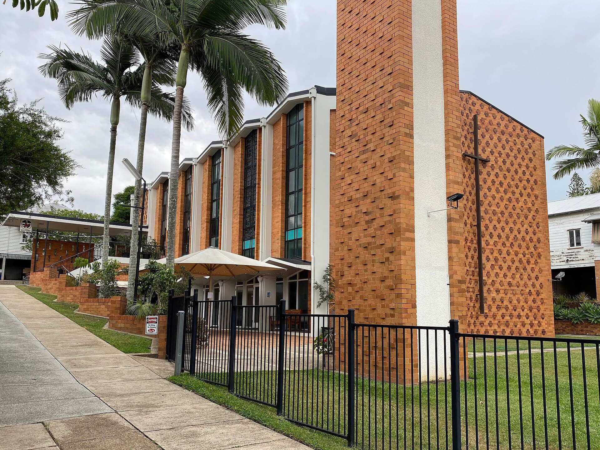 Black metal palisade fence along the street frontage of a mid-century brick church in Toowong, Brisbane, the sort of simple, see-through boundary older suburbs still recognise as a front fence.